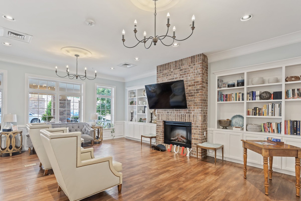 A stylish living room featuring a brick fireplace with a mounted TV, elegant chandeliers, and built-in bookshelves.