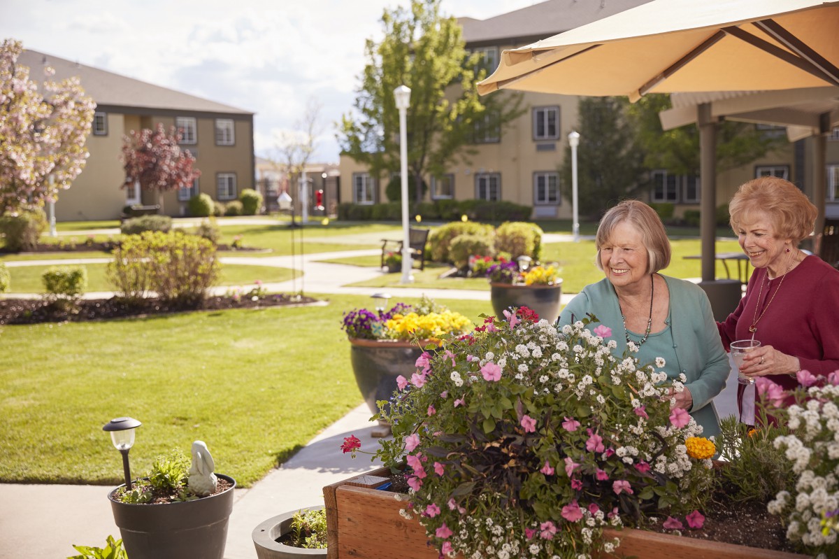A woman enjoying gardening in a sunny outdoor garden at a senior living community.