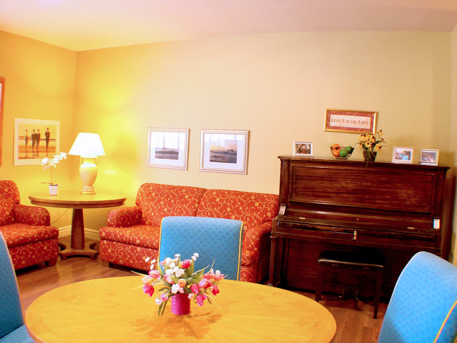A cozy living room with a sofa, piano, and a table adorned with flowers.
