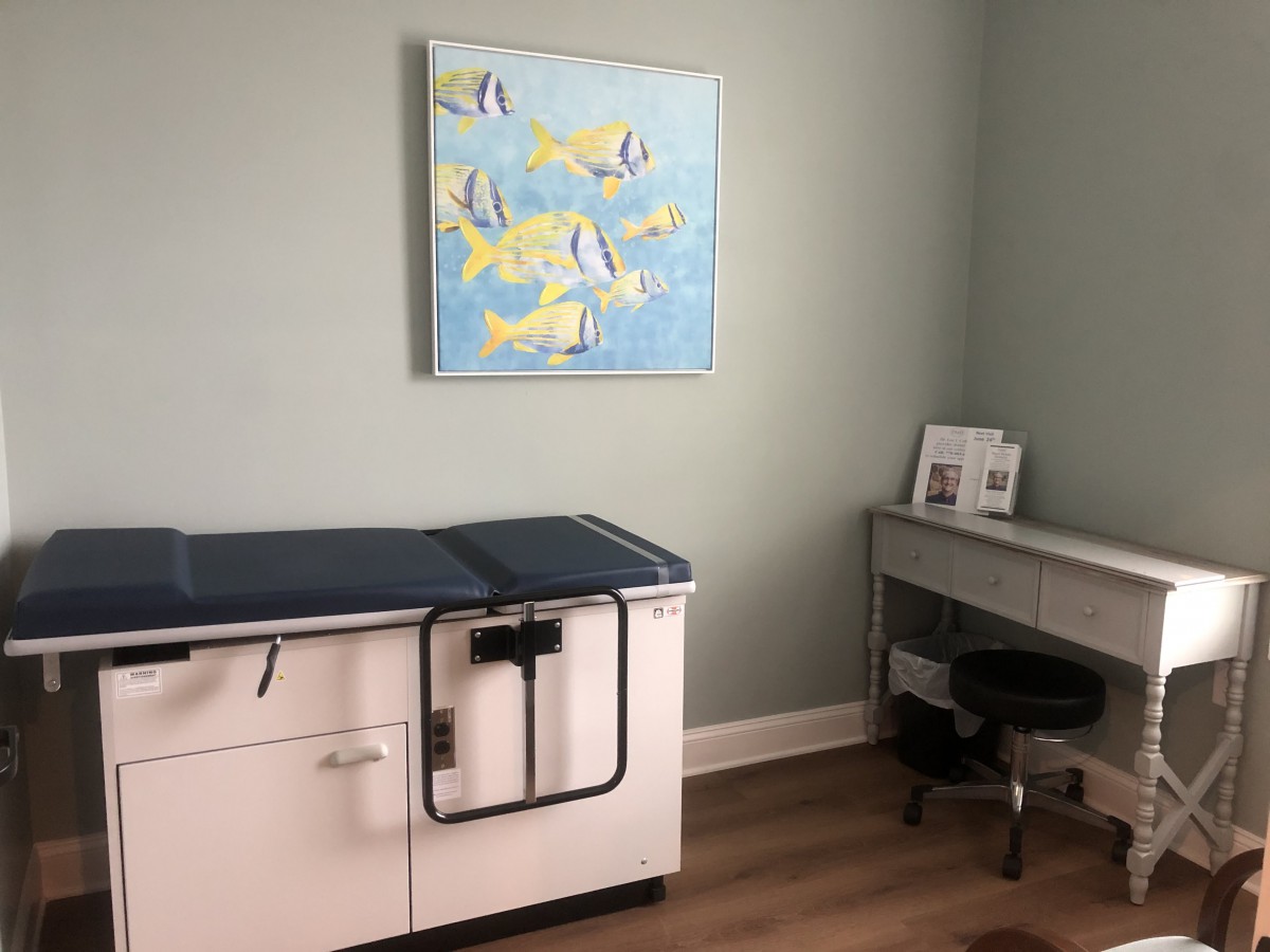 A clean and well-organized medical examination room with a painting on the wall.