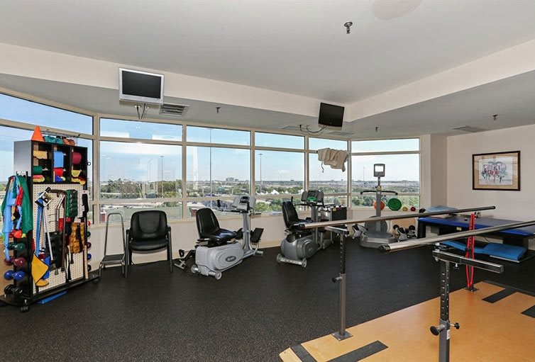 A well-equipped gym with treadmills and stationary bikes near large windows.