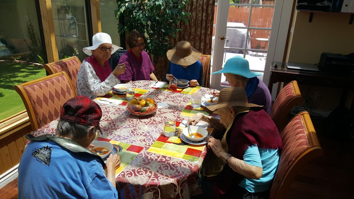 A group of elderly individuals wearing hats enjoy a meal together around a dining table indoors.
