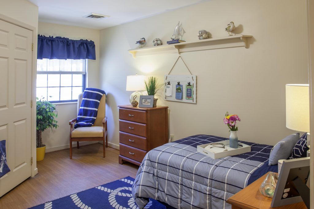 A cozy bedroom with a single bed, dresser, and window with blue curtains.