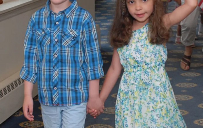A boy and a girl holding hands indoors, wearing casual clothing.
