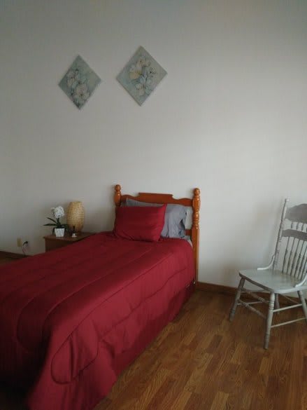 A simple bedroom with a single bed covered in red bedding, a wooden chair, and minimal wall decor.