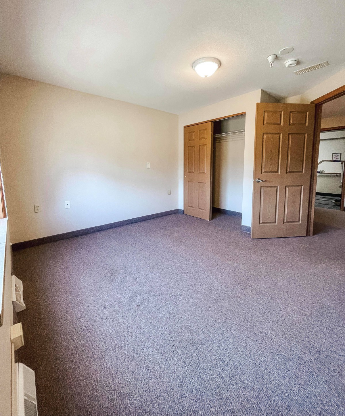An empty carpeted room with a closet and open door.
