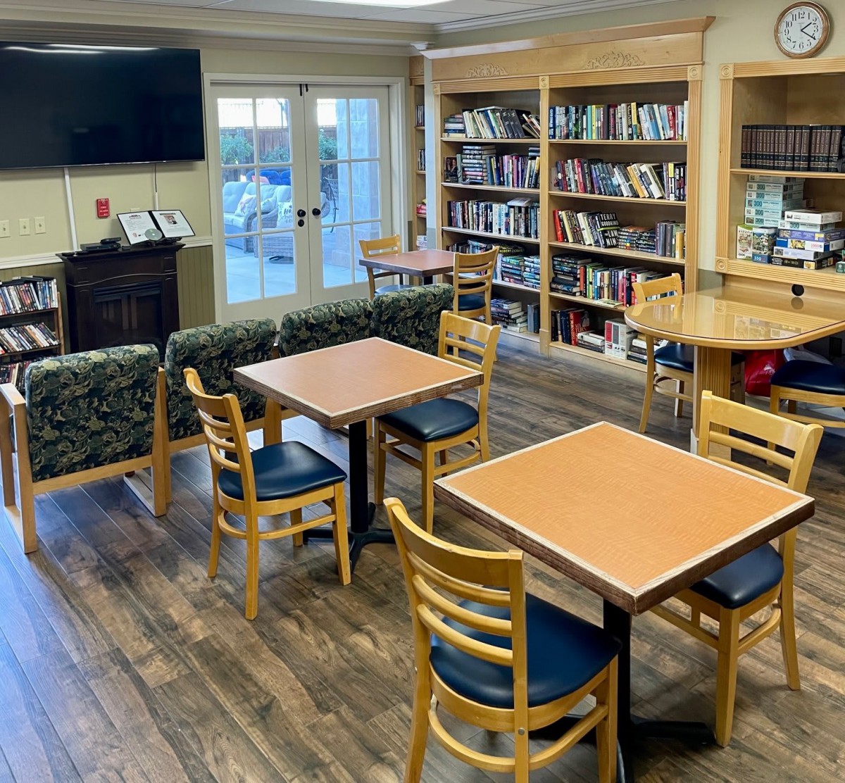 A cozy library room with bookshelves, tables, and a television.
