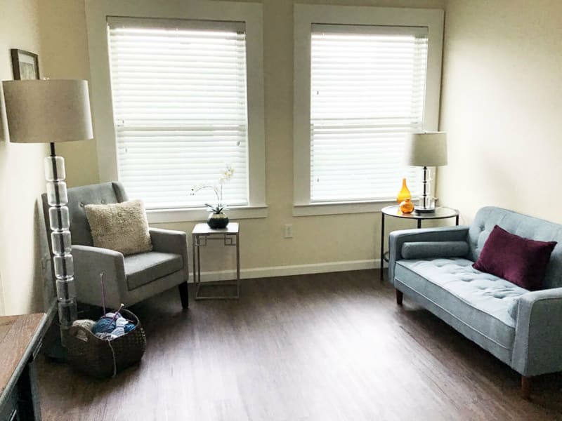 A modern and minimalist living room with a sofa, chair, and two large windows.