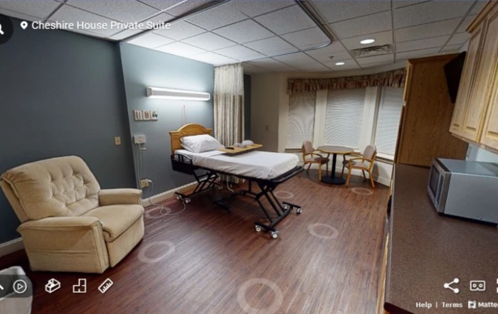 A hospital room with a patient bed, seating area, and large windows.
