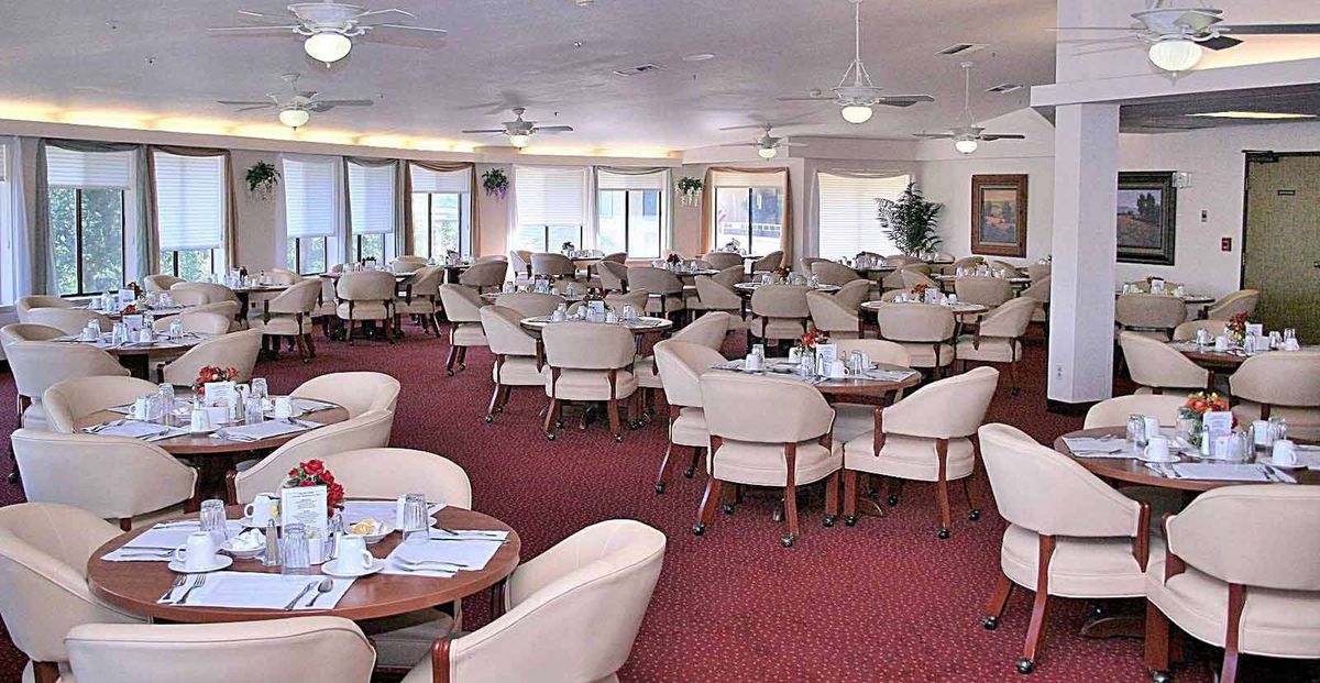 An empty indoor dining area with neatly arranged tables and chairs on a red carpet.