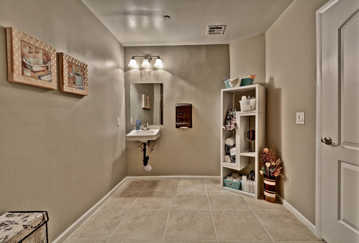 A tidy bathroom with a wall-mounted sink, mirror, and neatly organized shelving unit.