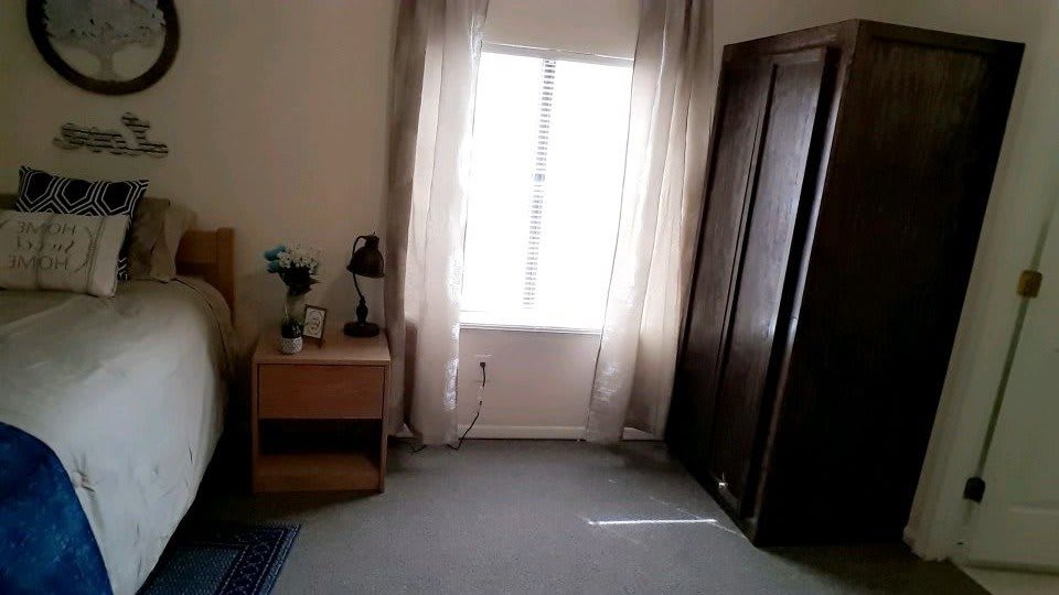 A bedroom with a window, curtains, nightstand, and closet.
