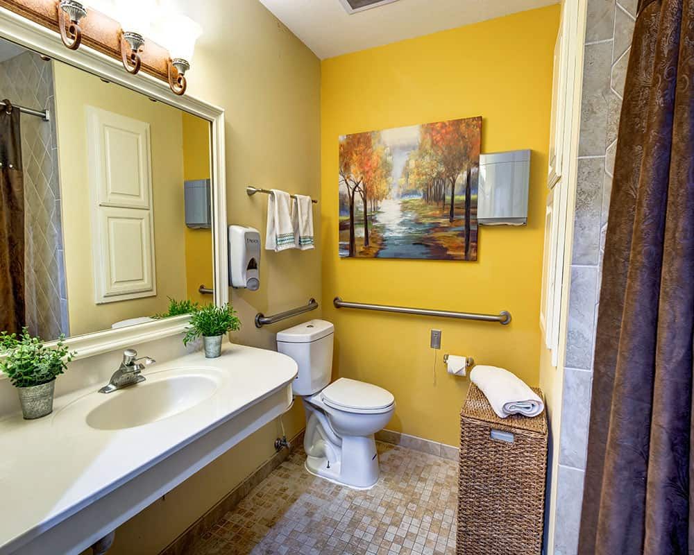 A well-decorated bathroom with a yellow accent wall, featuring a sink, toilet, and artwork.