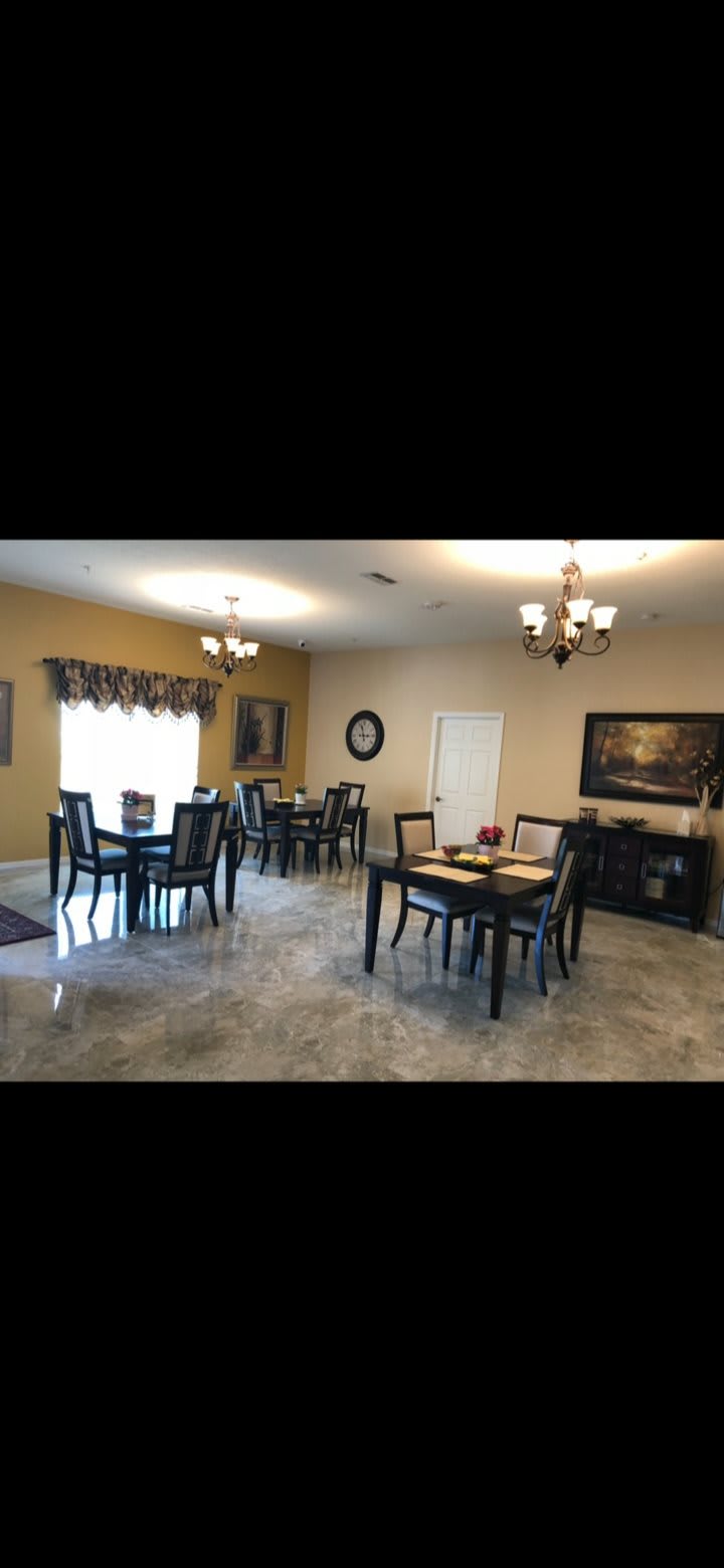 A spacious dining room with multiple tables and chairs, decorated with chandeliers and wall art.