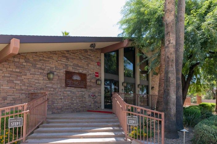 A brick building entrance with stairs and railings surrounded by trees.