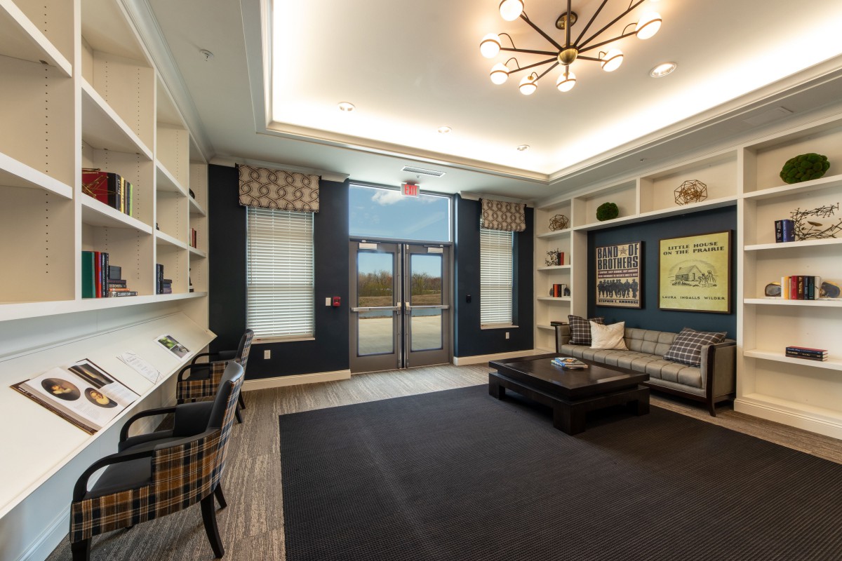 A modern lobby featuring a seating area with bookshelves, large windows, and a stylish chandelier.