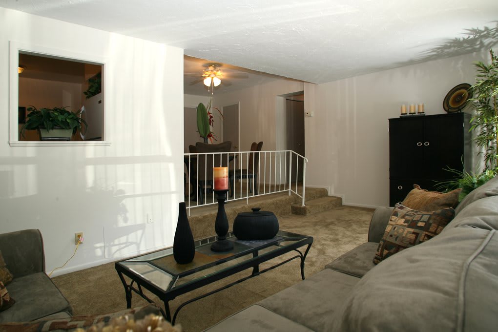 A cozy living room with a glass coffee table, decorative vases, and a view into the dining area.