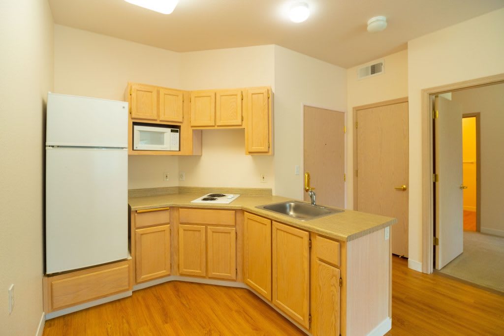 A compact kitchen featuring light wood cabinets, a refrigerator, microwave, and sink.