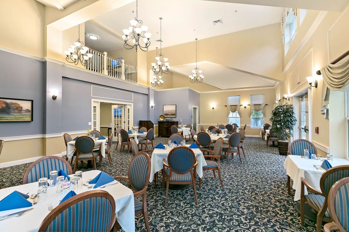 An elegant dining room with chandeliers, tables set with blue napkins, and a plush carpet.