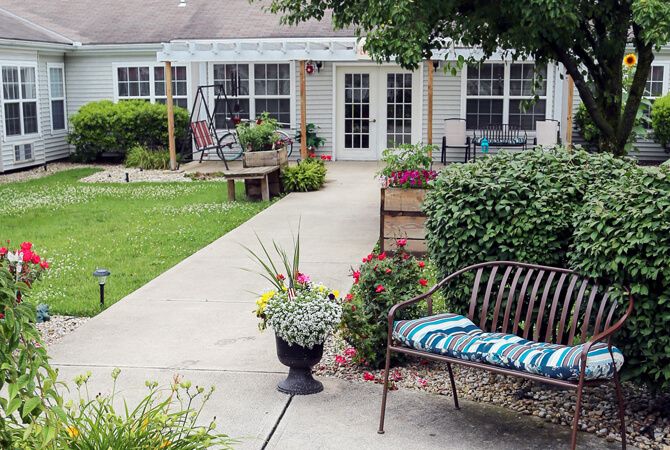 A charming garden patio with a pathway, featuring a bench and vibrant plants in pots.
