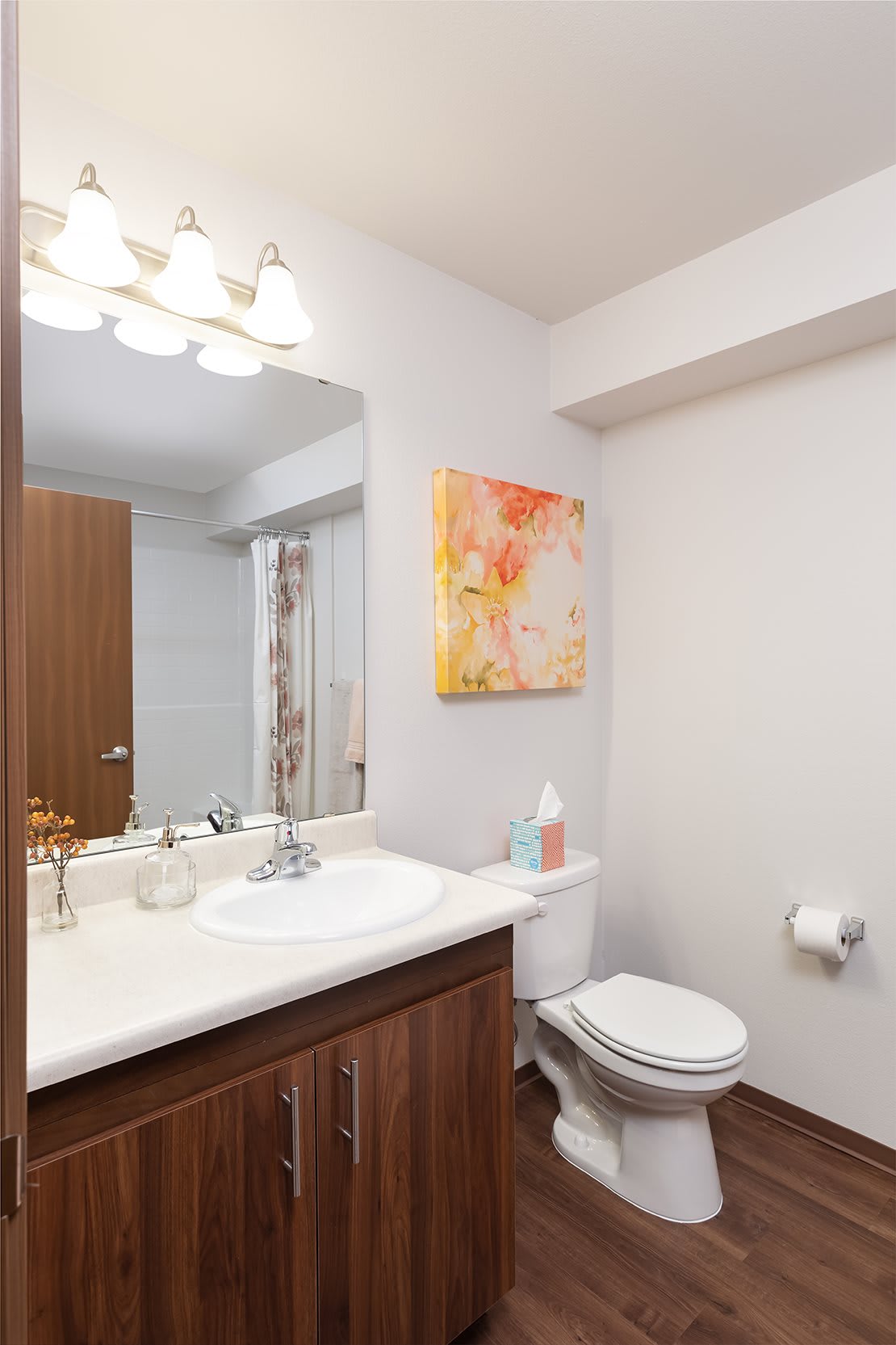 A modern bathroom featuring a sink with a mirror, toilet, and colorful artwork on the wall.