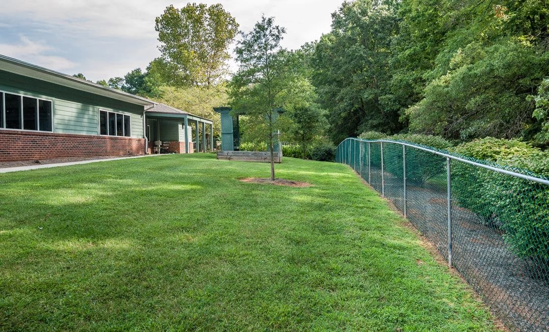 A well-maintained backyard with a lush green lawn, surrounded by trees and a chain-link fence adjacent to a house.