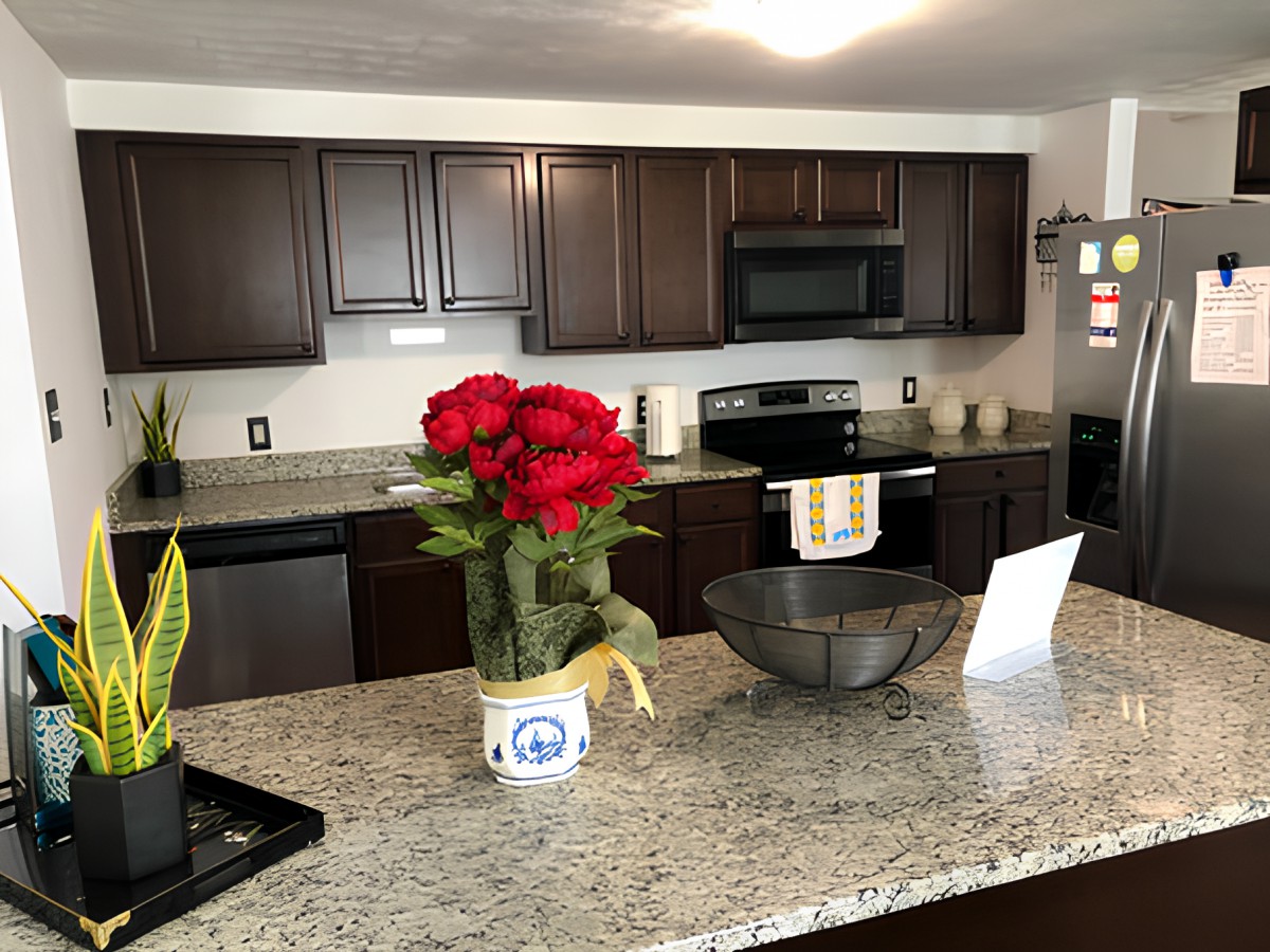 A modern kitchen with granite countertops and dark cabinetry, featuring decorative flowers and appliances.