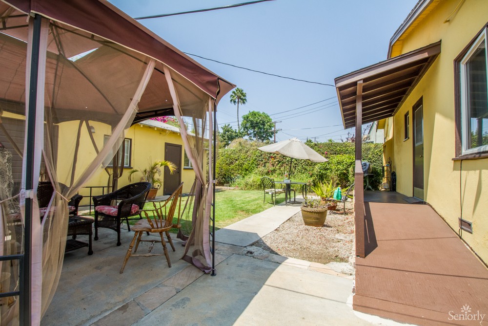 A cozy backyard featuring a patio with a gazebo and outdoor seating, surrounded by lush greenery on a sunny day.