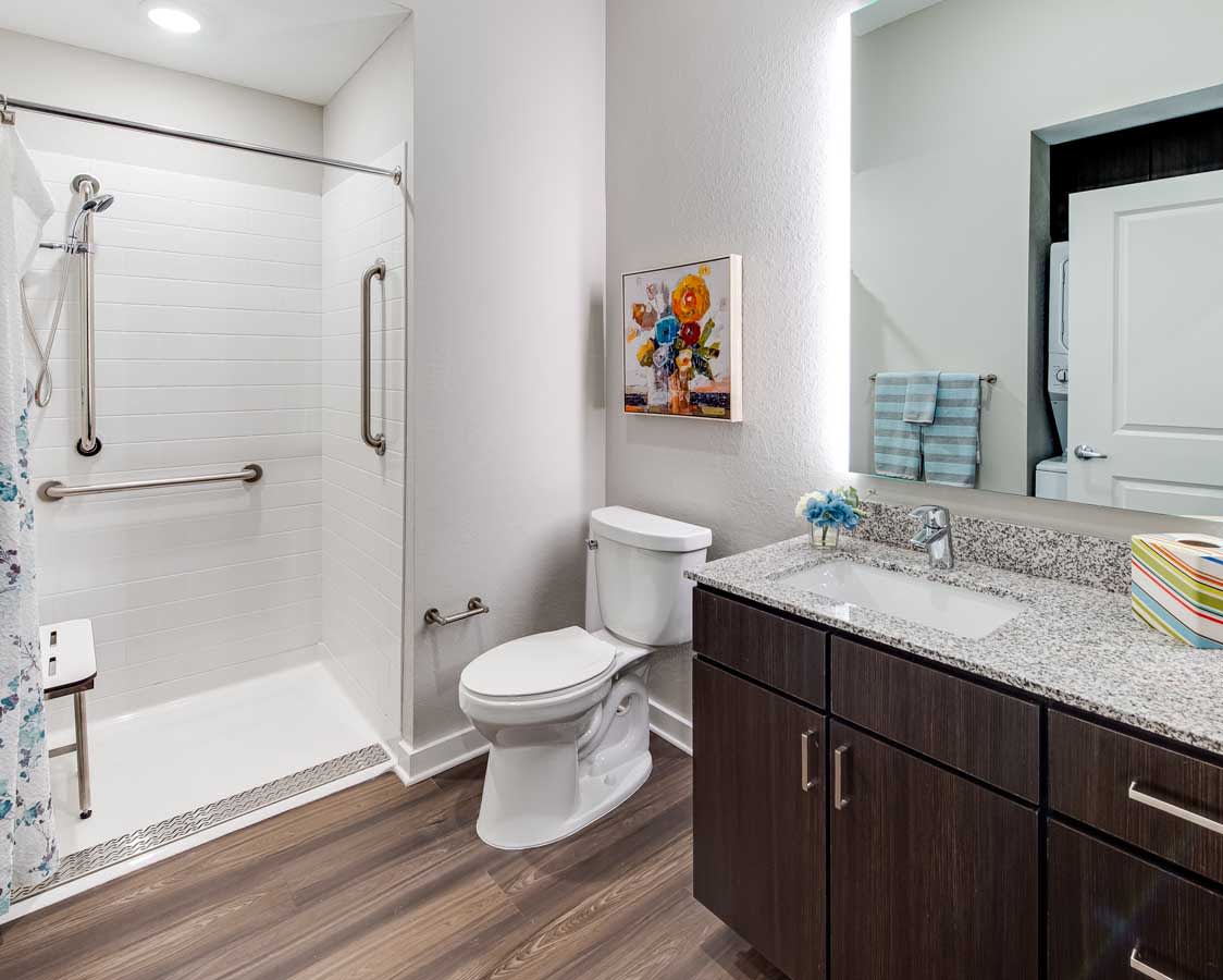 A modern bathroom with a walk-in shower, toilet, and vanity with granite countertop.