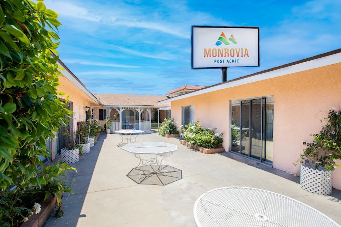 A sunny courtyard area of a motel with outdoor tables and a visible motel sign.