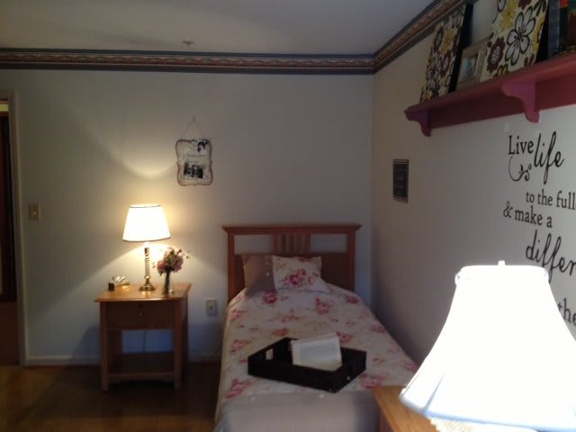 A cozy bedroom with a single bed, nightstand, and warm lighting.