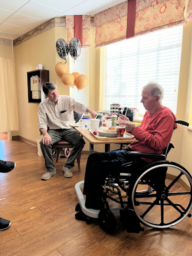 A caregiver engages with an elderly person in a wheelchair during a moment of connection.