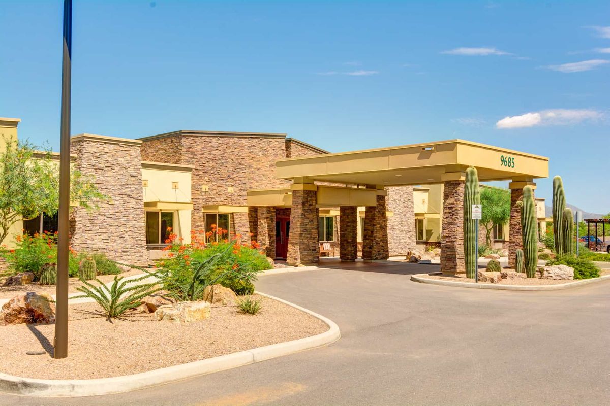 A modern building with a stone facade and desert landscaping, featuring cacti and a covered entrance.