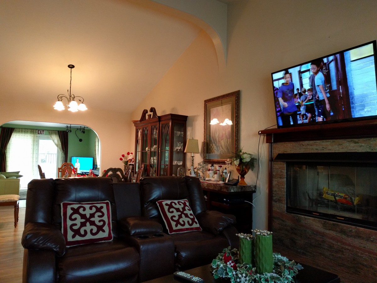 A cozy living room with a leather sofa, fireplace, and wall-mounted television, adjacent to a dining area.