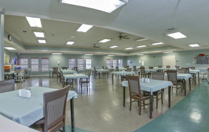 An empty dining hall with neatly arranged tables and chairs under bright lighting.