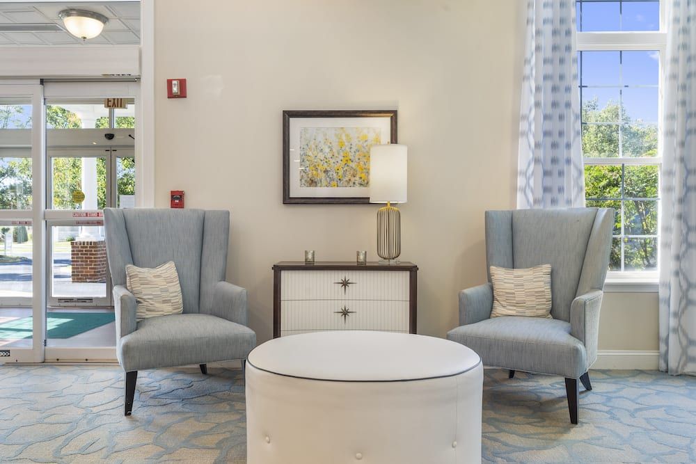 A cozy living room seating area featuring two armchairs and an ottoman, complemented by a lamp and artwork on the wall.