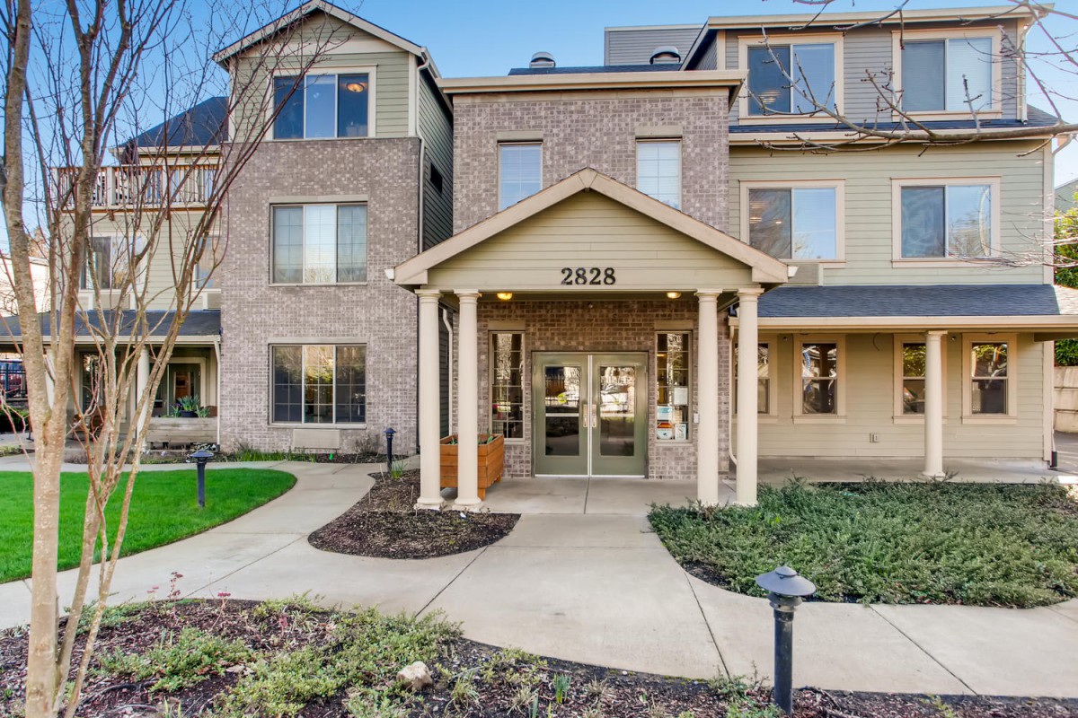 Entrance of a modern residential apartment building with brick exterior and landscaped walkway.
