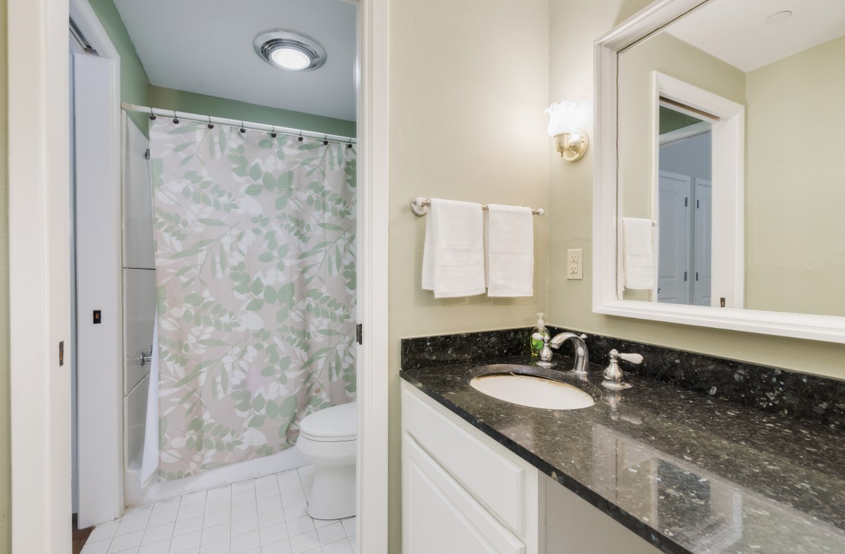 A modern bathroom with a black countertop, sink, mirror, and a shower area with a patterned curtain.