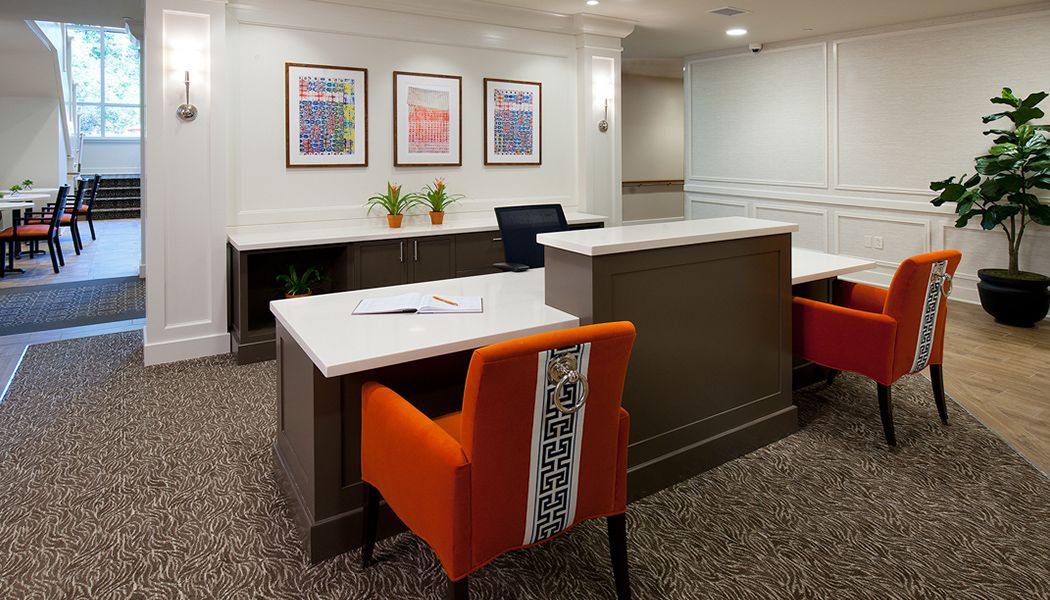 A modern reception area featuring a desk, vibrant orange chairs, and framed artwork on the wall.