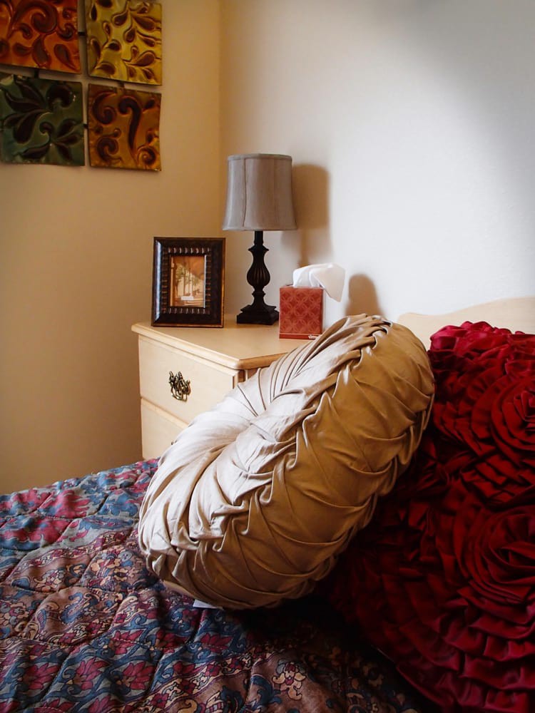 A cozy bedroom corner with a bedside table, decorative pillows, and a lamp.