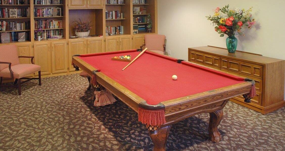 A cozy game room featuring a pool table with red felt and a cue stick resting on top.