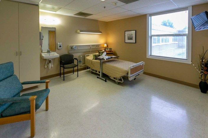 A hospital room with a single bed, chairs, and medical equipment.