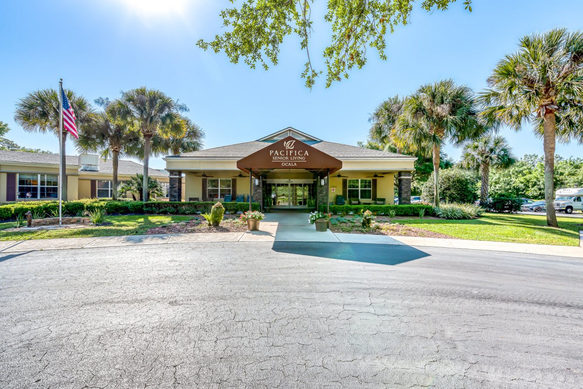 A sunny day view of a building entrance surrounded by palm trees and landscaped greenery.