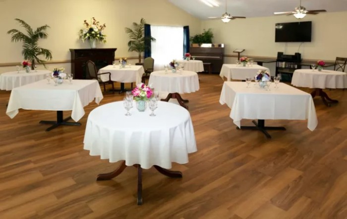 An elegantly set dining room with round tables covered in white tablecloths and decorated with flowers.