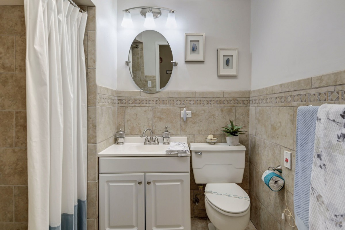 A small, neatly arranged bathroom with a toilet, vanity sink, and shower area.