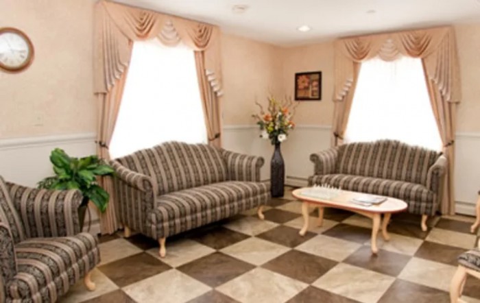 A cozy living room featuring striped sofas, a coffee table, and checkered flooring, adorned with curtains and decorative plants.