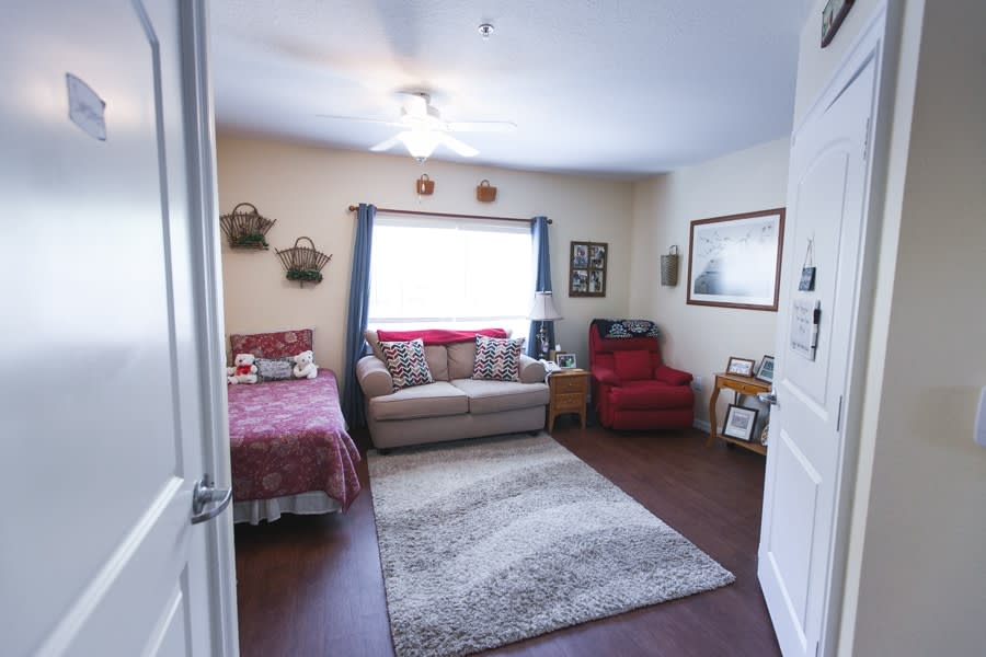 A cozy bedroom with a sofa, bed, and armchair, complemented by a large rug and wall decorations.
