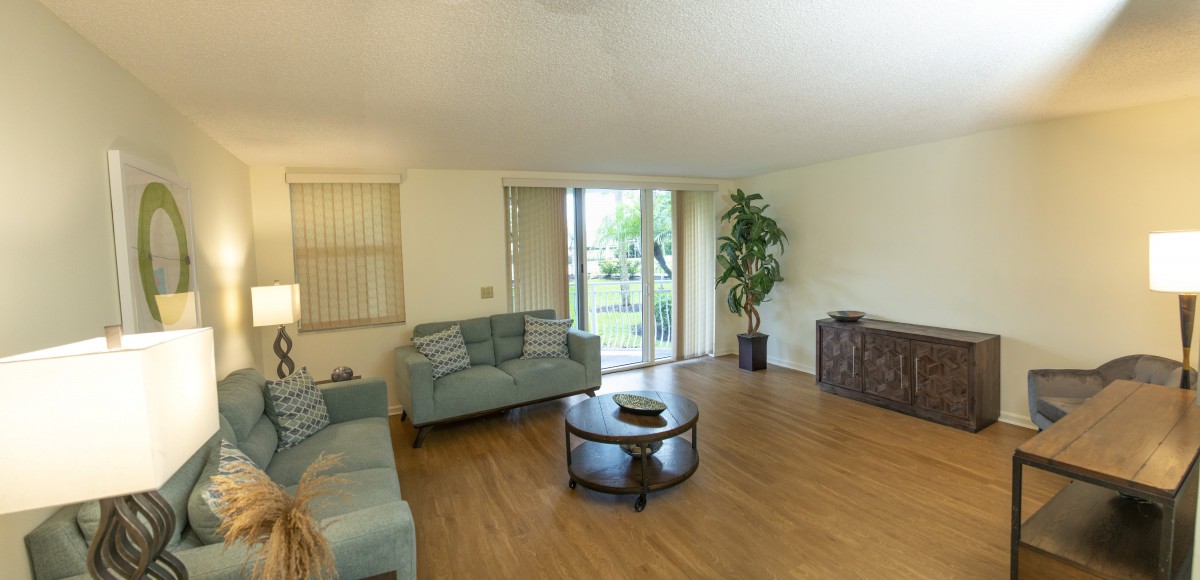 A spacious living room with a modern sofa, a round coffee table, large windows providing natural light, and a potted plant in the corner.