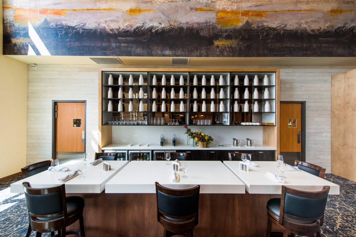A modern restaurant interior featuring a bar with seating and neatly arranged shelves of glasses.