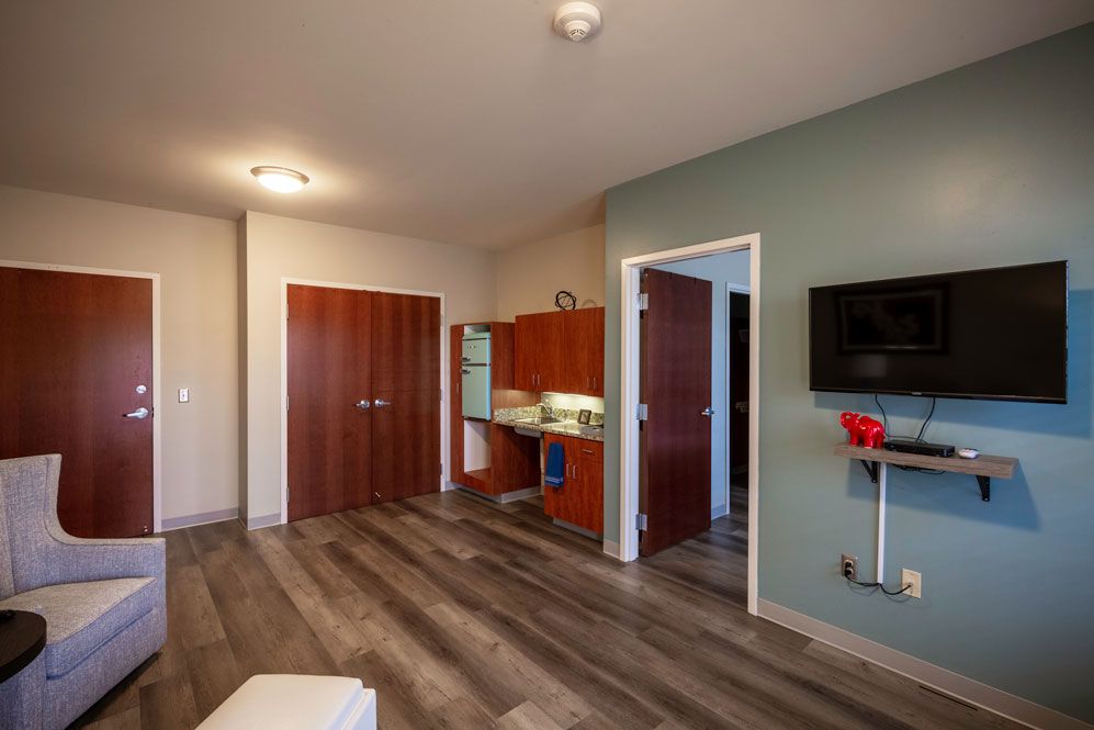 A modern apartment interior featuring a small kitchen, wood flooring, and minimalist furniture.